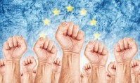 Europe Labour movement, workers union strike concept with male fists raised in the air fighting for their rights, European Union flag in out of focus background.